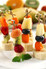 Fresh fruits on skewers in plate on table, closeup