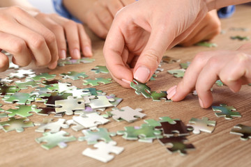 Fototapeta premium Female hands assembling puzzle on wooden table, closeup