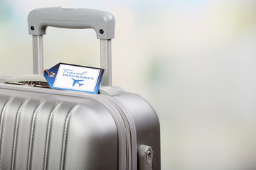Suitcase with TRAVEL INSURANCE label on light blurred background