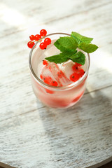 Glass of cold refreshing summer drink with berries and ice cubes on table close up