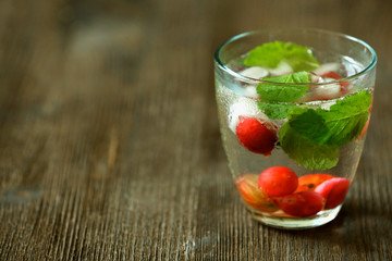 Glass of cold refreshing summer drink with berries and ice cubes on table close up