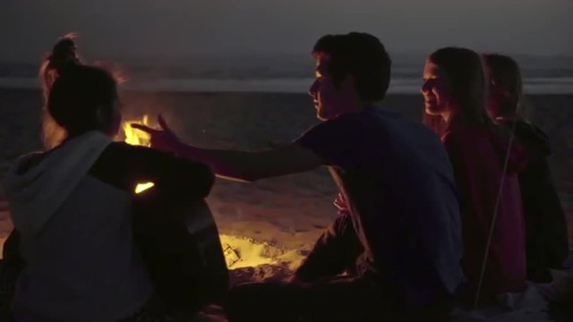 Over the shoulder shot of attractive teenagers sitting around a fire by the beach 