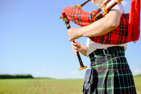 Male playing Scottish traditional pipes on green summer outdoors