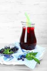 Glass jug of fresh blackcurrant juice on checkered napkin on wooden background