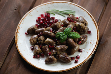 Glass plate with roasted chicken hearts over dark wooden surface