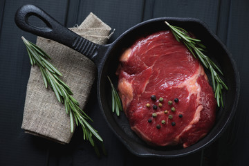 Above view of raw ribeye steak with rosemary in a frying pan