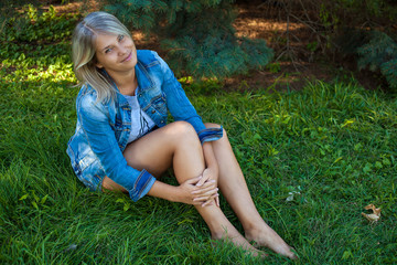 Posing beautiful girl sitting on the lawn in the park; outdoors.