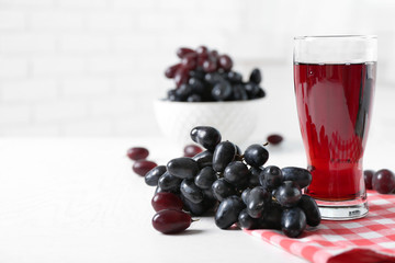 Glass of juice and ripe grapes in bowl on wooden table