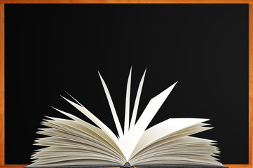 Openned book over blank blackboard with wood frame