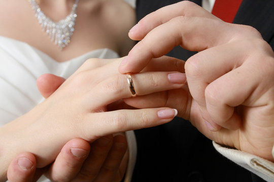 hand of groom putting a ring on finger of his bride