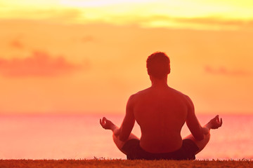 Meditation and Yoga. Rear view of young man meditating in lotus position. Male is practicing yoga at beach. He is doing relaxation exercise at beach during sunset. - obrazy, fototapety, plakaty