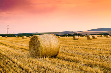 Golden sunset over farm field with hay bales