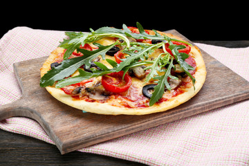 Tasty pizza with vegetables and arugula on cutting board on table close up