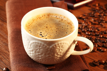 Cup of fresh coffee with beans on table, closeup