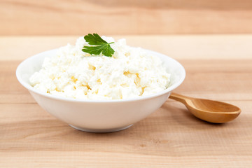 Fresh cottage cheese in a white bowl with wooden spoon.