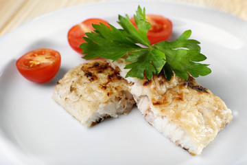 Dish of fish fillet with parsley and tomato on plate close up