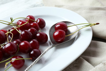 Sweet cherries on plate, on wooden background