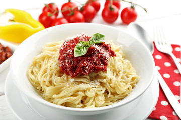 Spaghetti with tomato sauce and cheese on white plate, on color wooden background