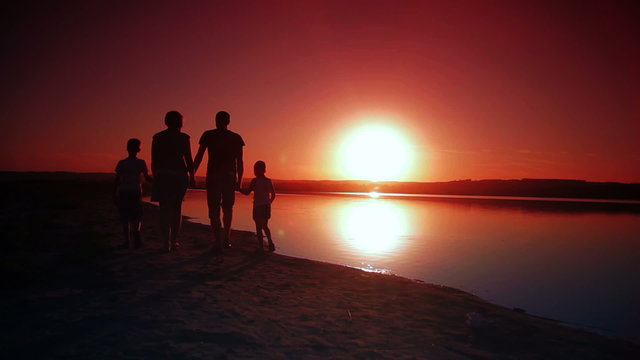 4 person family walking on the beach holding hands at sunset