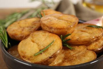 Delicious baked potato with rosemary in bowl on table close up