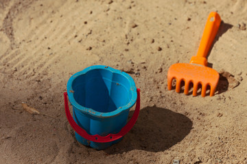 Fototapeta na wymiar In the sandbox. / Bucket and rake in the sand.