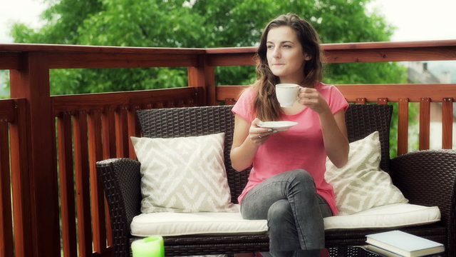 Girl drinking coffee and smiling to the camera on the terrace
