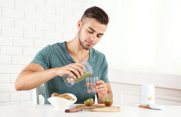 Obraz na płótnie Canvas Young man man pouring fresh kiwi juice into glass