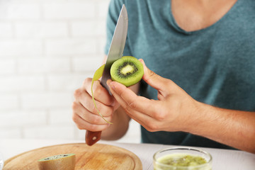 Young man peeling kiwi, preparing orange juice