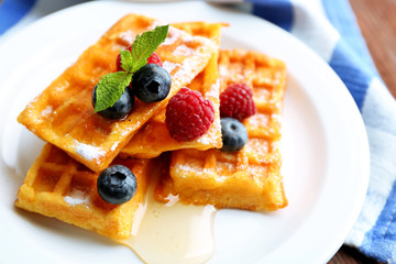 Sweet homemade waffles with forest berries and sauce on table background