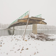 Square landscape of an angled view of a flood damaged bridge in winter.