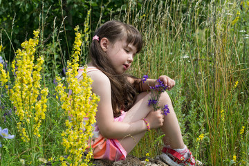 Little girl sits on a rock and looks at a flower