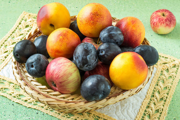 A lot of plums, apples and nectarines in a wicker basket