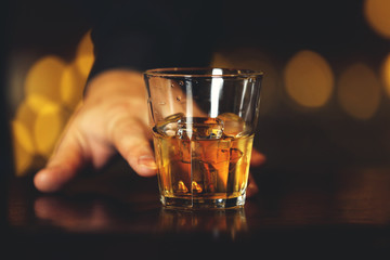 Whiskey glass tumbler in male hand on bar counter