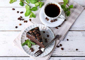 Delicious chocolate cake with mint and cup of coffee on table close up