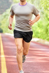 Low section of determined man running on country road. Young male is in sports clothing. He is representing fit and healthy lifestyle.