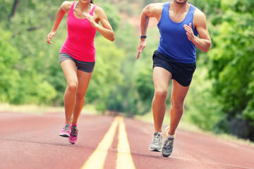 Low section of determined man and woman running on country road. Young couple is in sports clothing. They are representing their healthy lifestyle. - Powered by Adobe