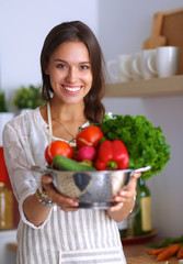 Smiling young woman holding vegetables standing in kitchen