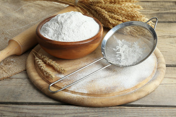 Whole flour in bowl with wheat ears on wooden table, closeup