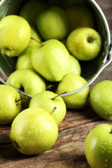 Ripe green apple in metal bucket on wooden table close up