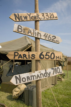 World War II replica signs to New York, London, Berlin and Normandy with mileage totals in front of tents at Mid-Atlantic Air Museum World War II Weekend and Reenactment in Reading, PA held June 18, 2009
