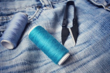 Fototapeta na wymiar Bobbins threads with scissors on jeans