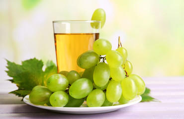 Glass of grape juice on wooden table on light blurred background
