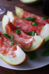 Melon with prosciutto of Parma ham on wooden table, closeup