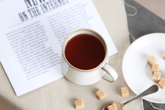 Cup of flavored coffee with lump sugar on table with napkin and newspaper, closeup