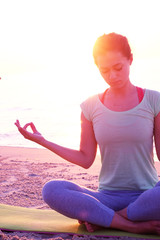 Young healthy woman practicing yoga on the beach at sunset