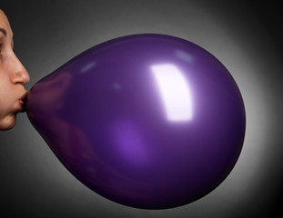 Young woman inflating balloon on gray background