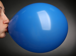 Young woman inflating balloon on gray background