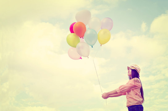 Girl hand holding multicolored balloons done with a retro vintage instagram filter effect, concept of happy birth day in summer and wedding honeymoon party (Vintage color tone paper texture)