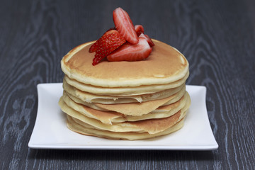 Stack of pancakes with cut strawberry on dark wooden background