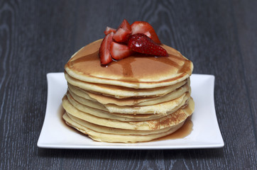 Stack of pancakes with strawberry on dark wooden background